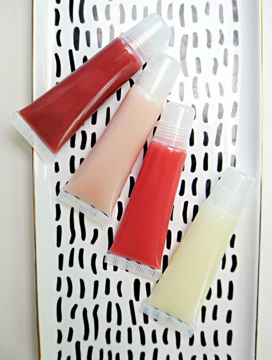 4 lip gloss tubes of different colors laying on black and white tray