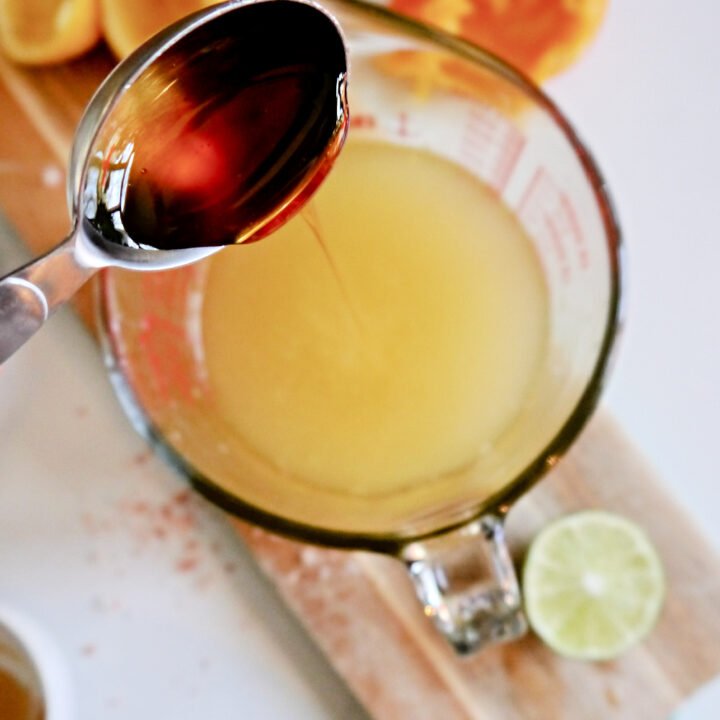 Measuring cup pouring honey into a bowl of citrus liquid