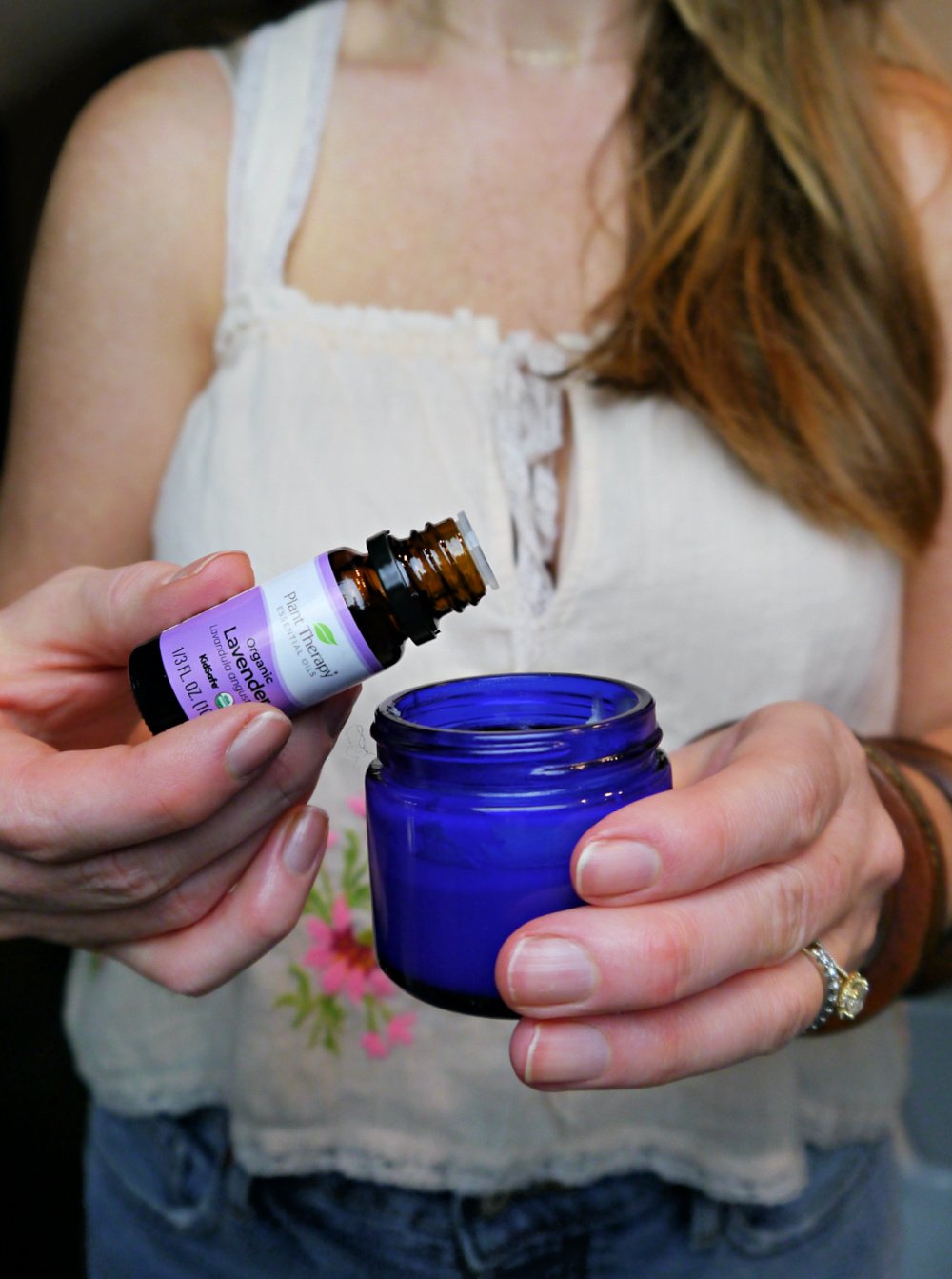 Woman dripping lavender essential oil into a blue jar.