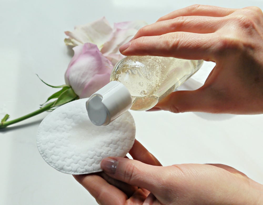Hands pouring DIY face toner on a cotton oval