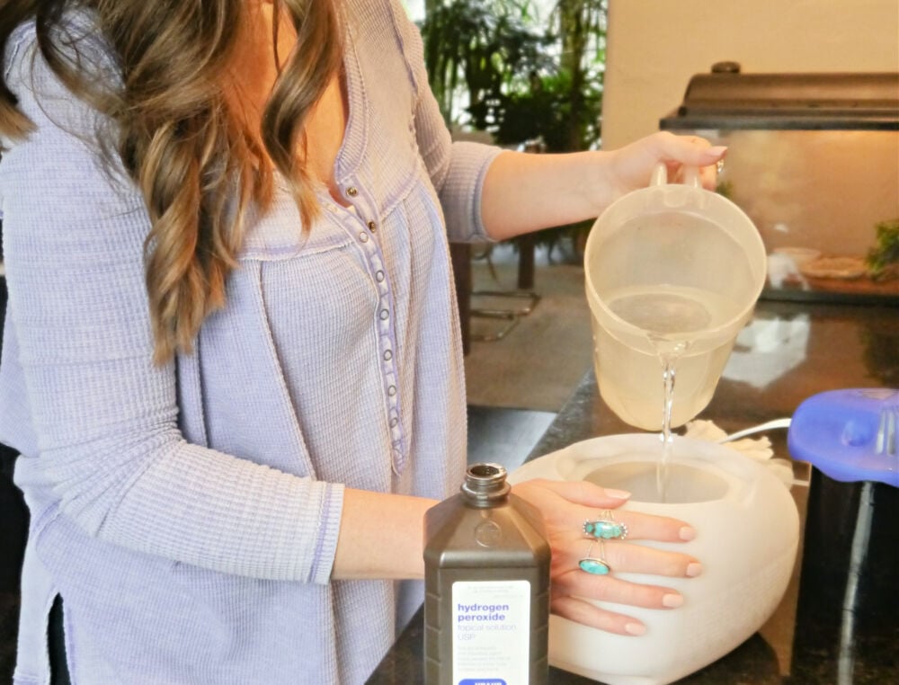 Woman pouring hydrogen peroxide and water into a humidifier.