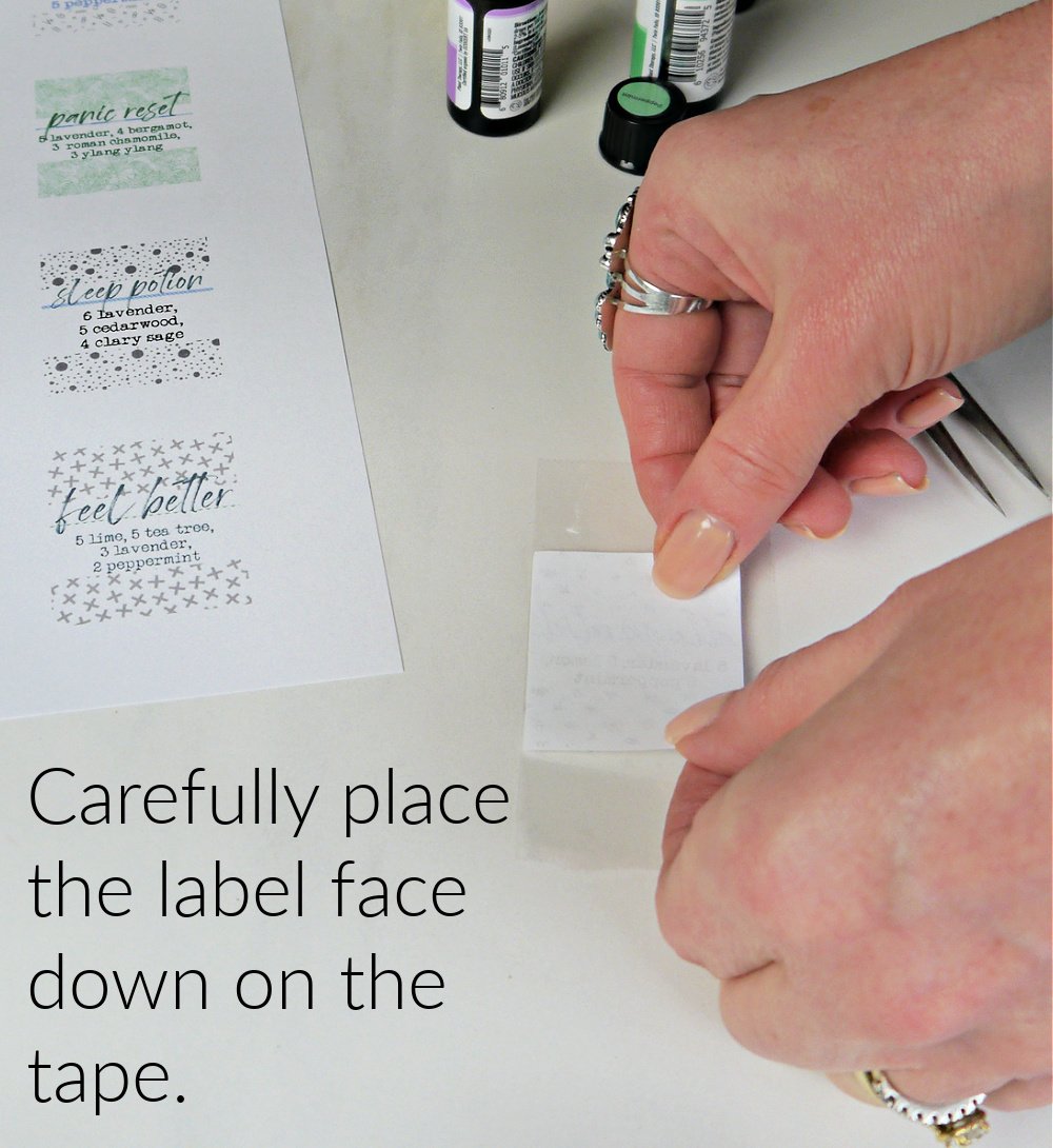 Hands placing label face down on the sticky side of the tape. 