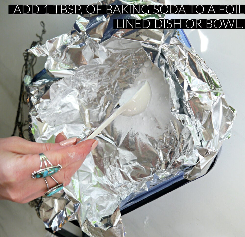 A foil covered dish with a hand dumping a tablespoon of baking soda in.