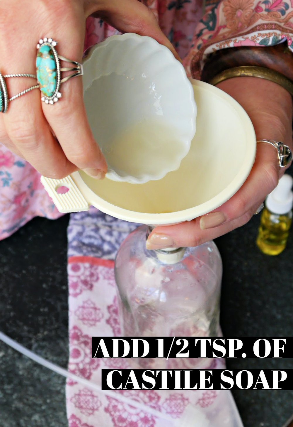 Hand pouring Castile soap into a funnel on a glass spray bottle.