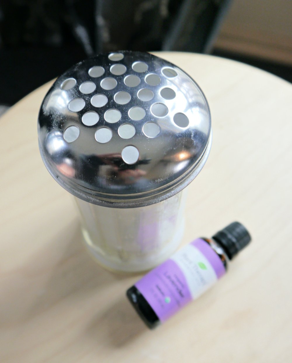 Shaker jar with baking soda and lavender essential oil on a table.