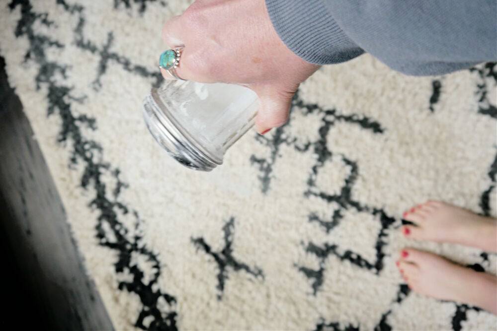 Hand sprinkling baking soda over carpet.